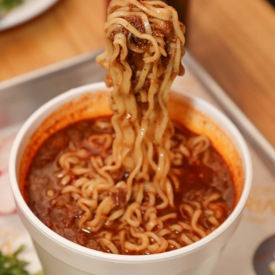 Close-up of noodles lifted from a bowl of spicy red broth with meatballs.